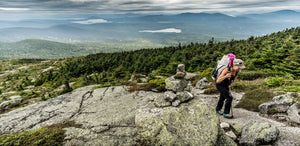 A woman carrying a baby on a rocky mountain top.