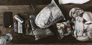 The contents of a backpack are laid out on a wooden table.
