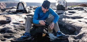 A man is sitting on a rock and drinking water.