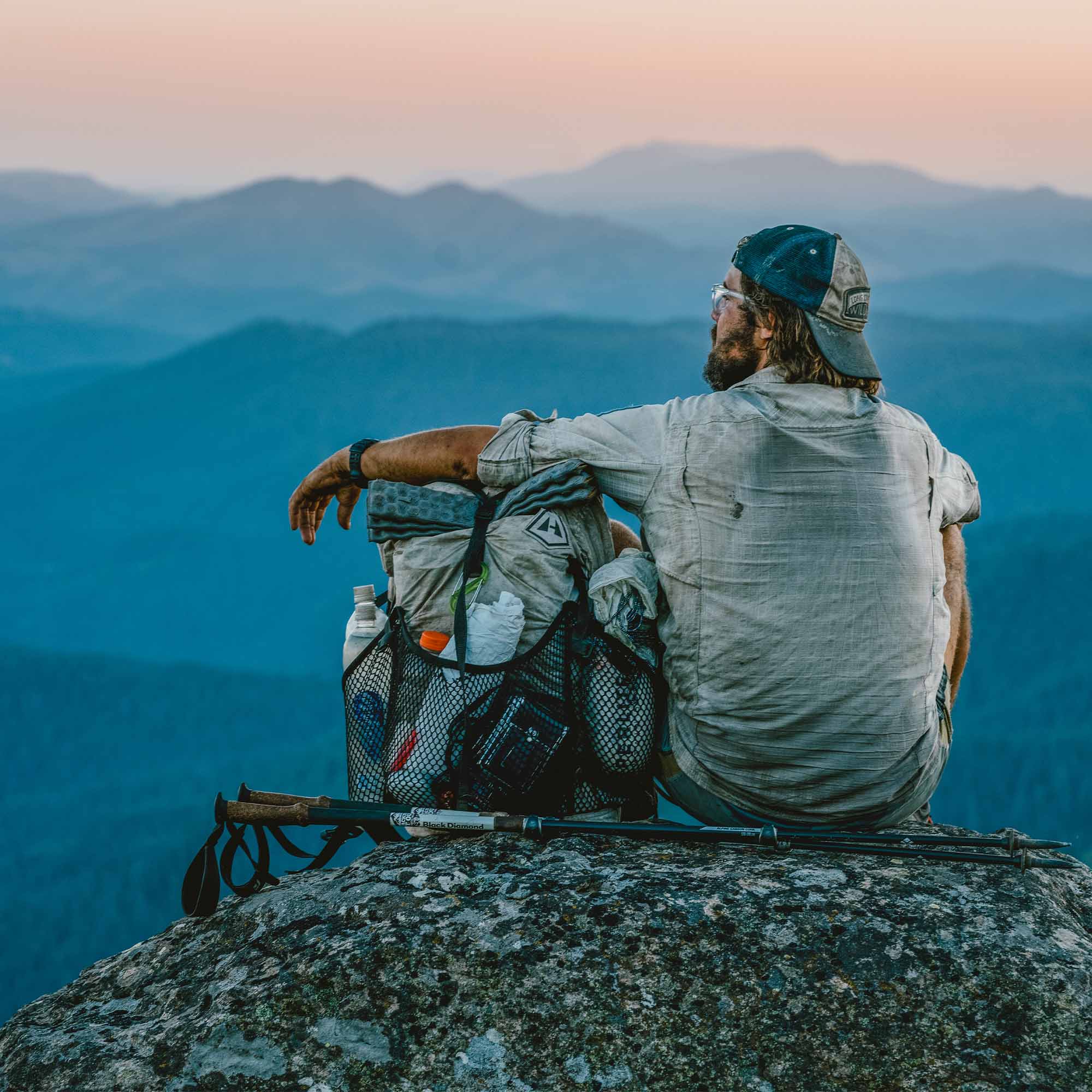 A man sitting on top of a mountain looking at the mountains.