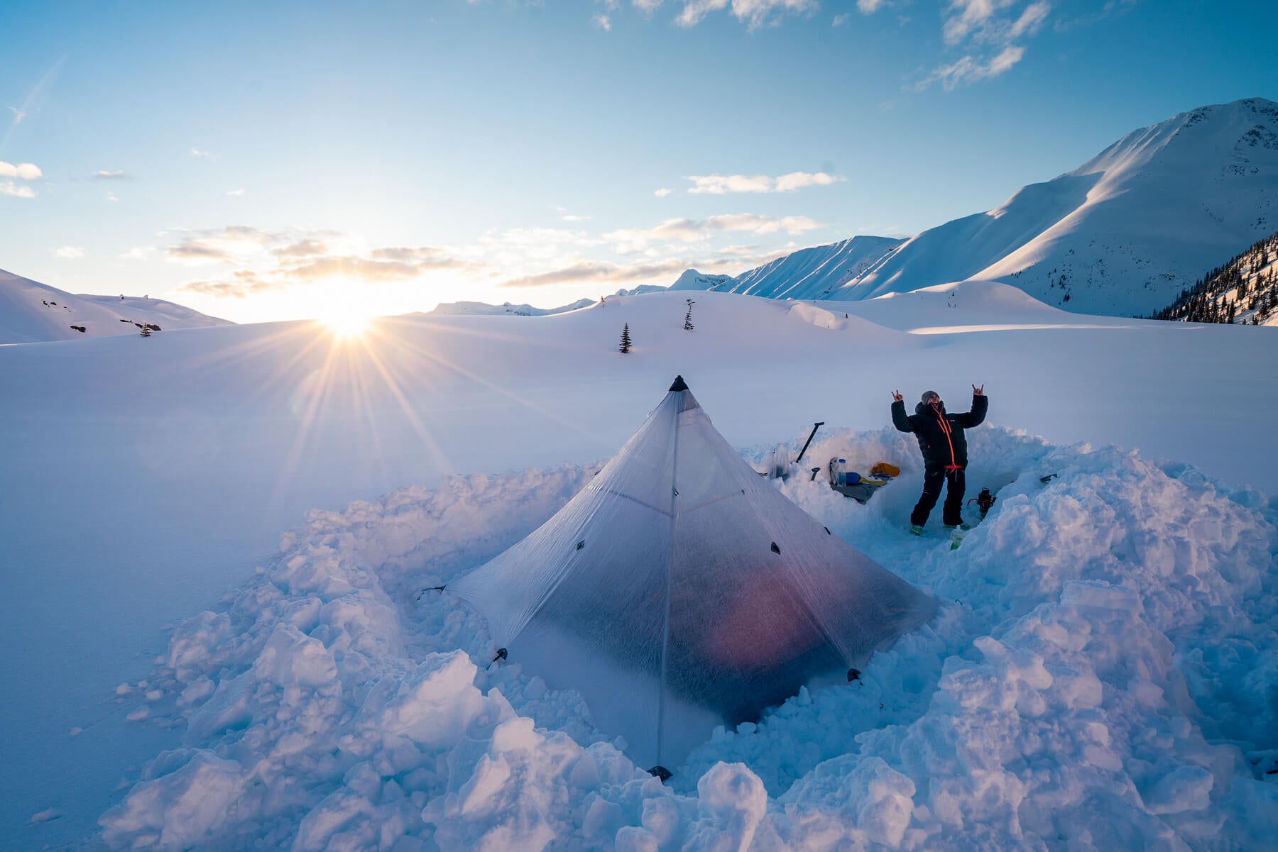 A person standing next to a tent in the snow.
