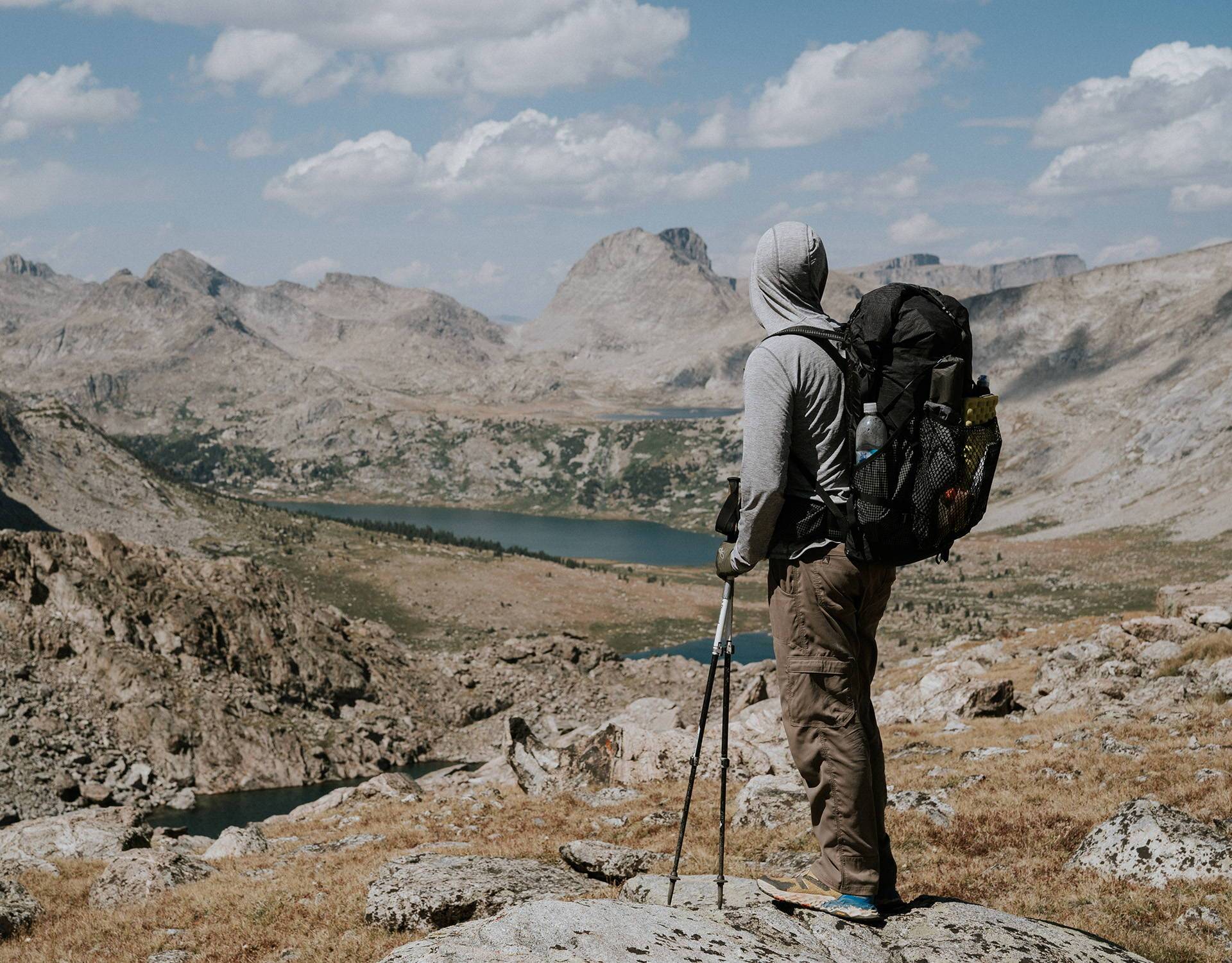 A man with a backpack standing on top of a mountain overlooking a lake.