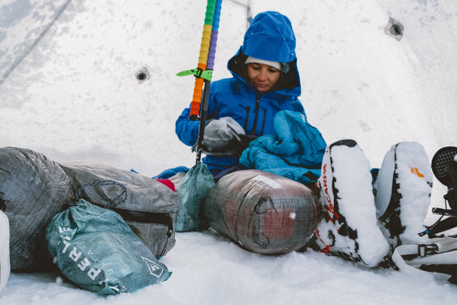 A man in a blue jacket sits in a snow tent.